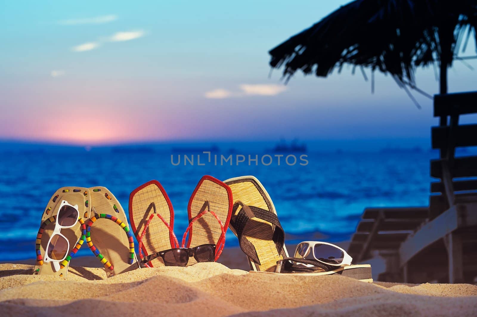 Three pair of beach sandals and glasses on the beach