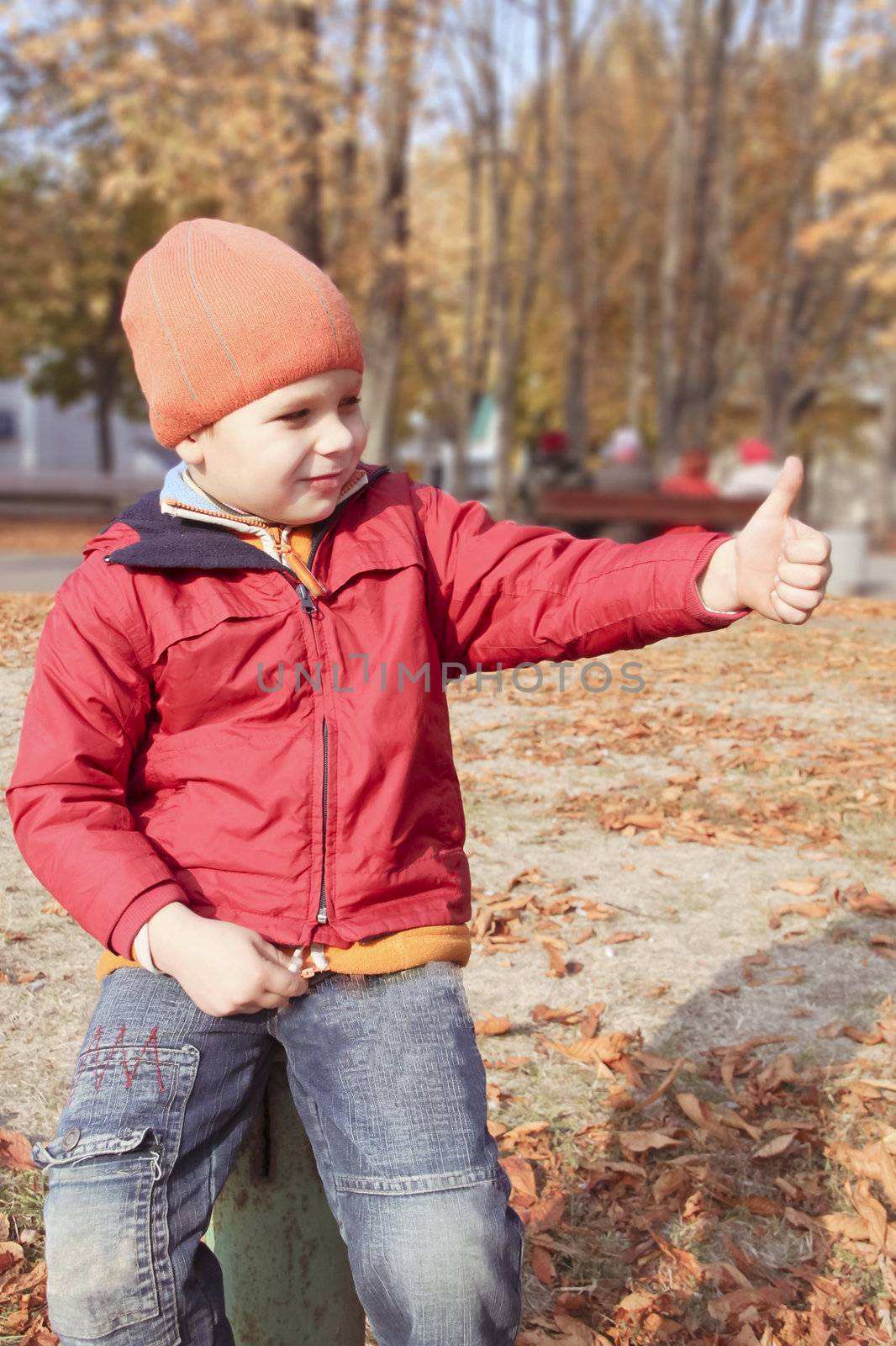 Happy kid shows up finger, sitting in autumn park