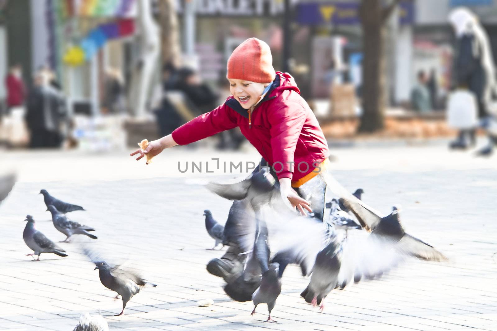 Happy kid playing with pigeons in a city park by NickNick