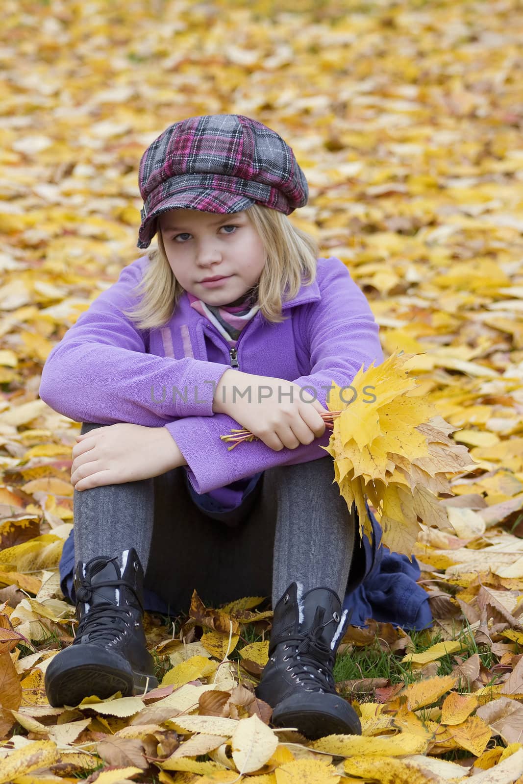 little girl sitting on leaves in the park by miradrozdowski