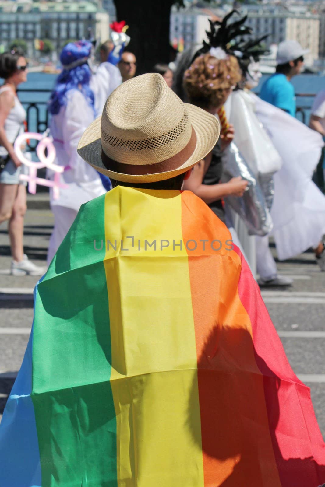 Person wearing a hat made of straw and a big rainbow flag while watching and participating at the Gaypride