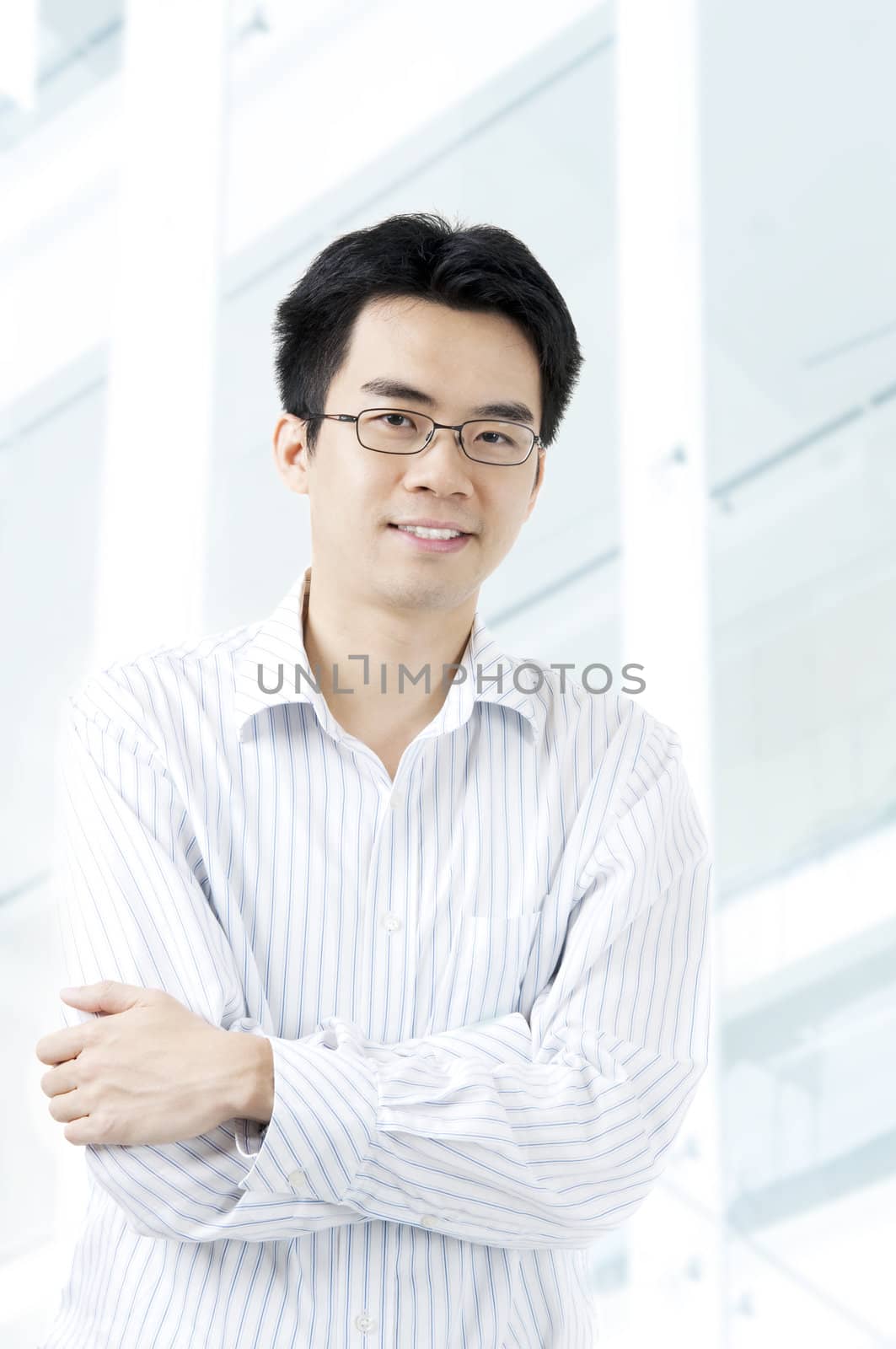 Good looking Asian business man standing with arms folded, building at background.