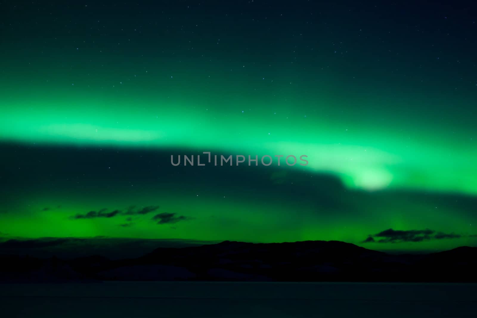 Green northern lights (aurora borealis) substorm above silhouette of hills and clouds.