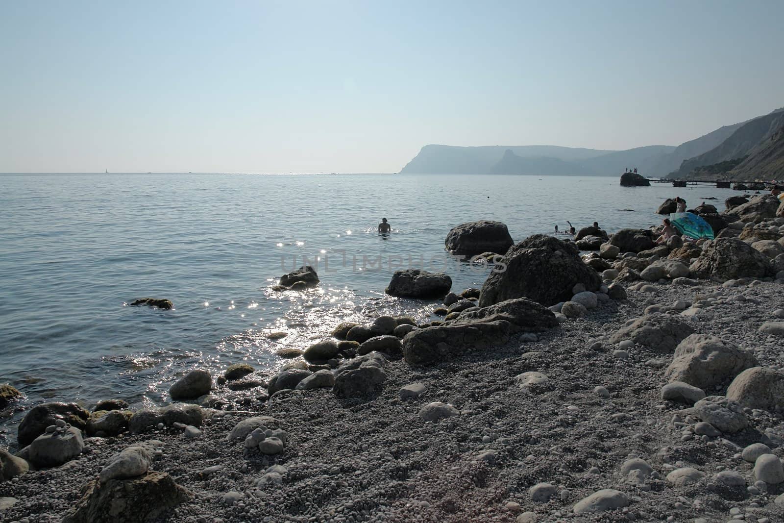 Noon. Stony beach. Sun is reflected in the sea.