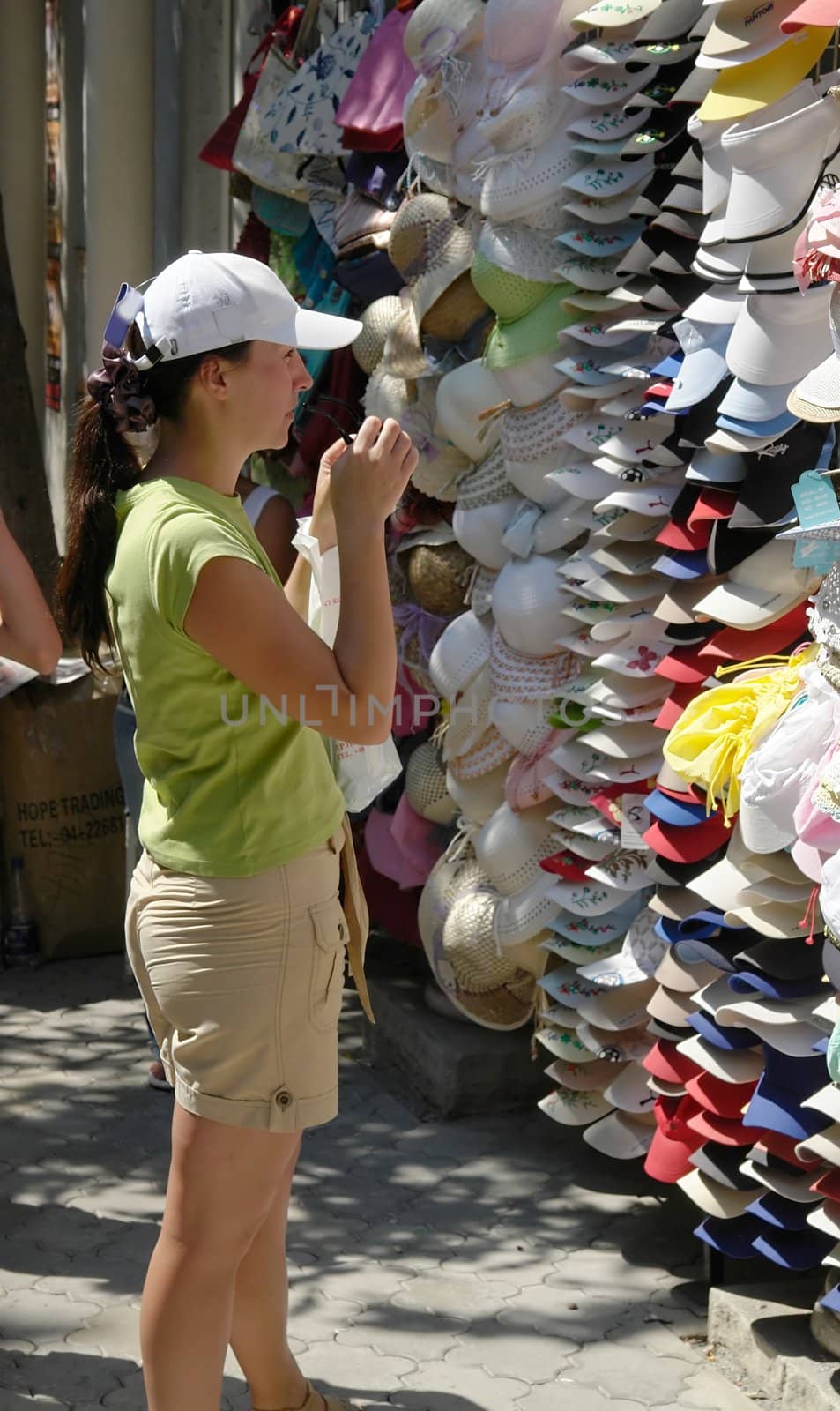 Young woman selects cap on the market.