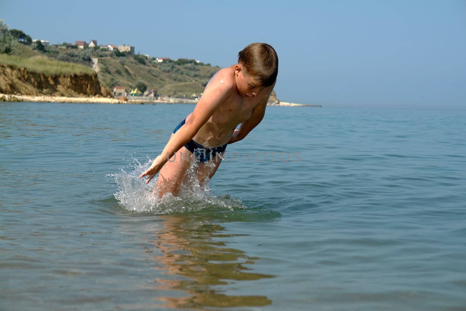 Young boy jumping into wave on a sunny beach