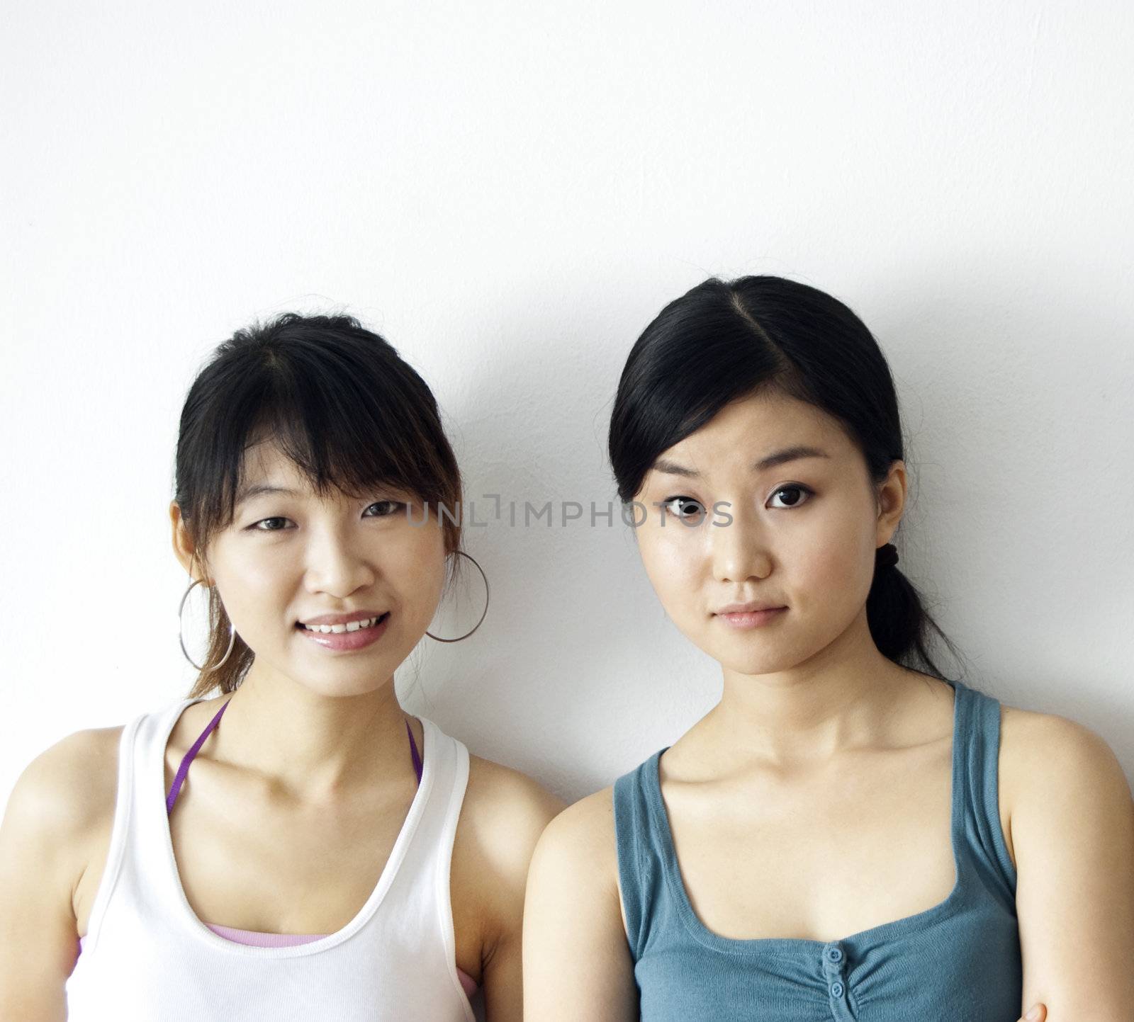Portrait of two Asian girls leaning on wall