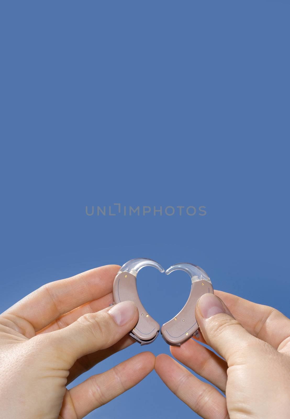 Hands showing a heart shape from digital hearing aids in fron of a blue sky background useful for text