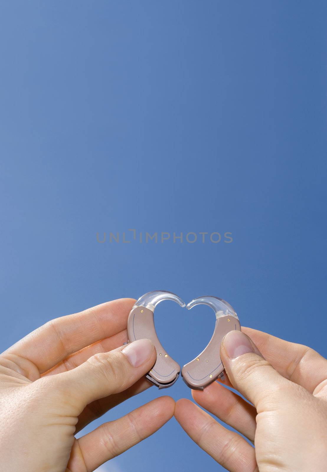 Hands showing a heart shape from digital hearing aids in fron of a blue sky background useful for text