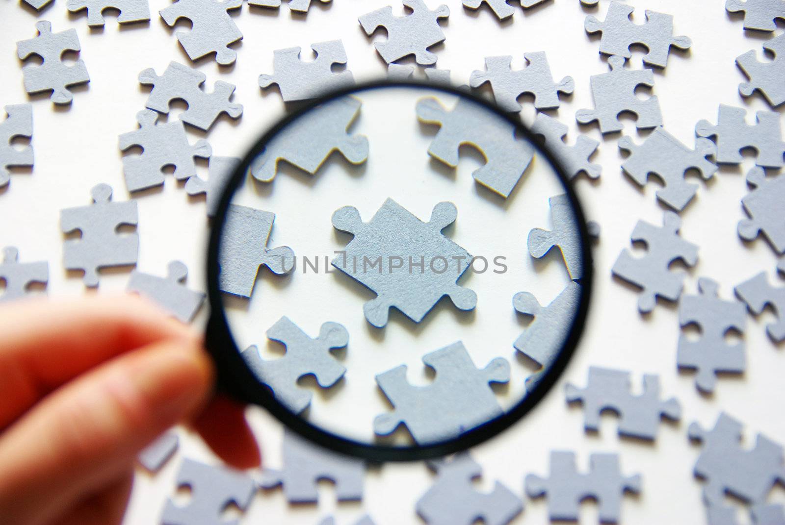 Hand with magnifying glass and puzzle isolated on white background