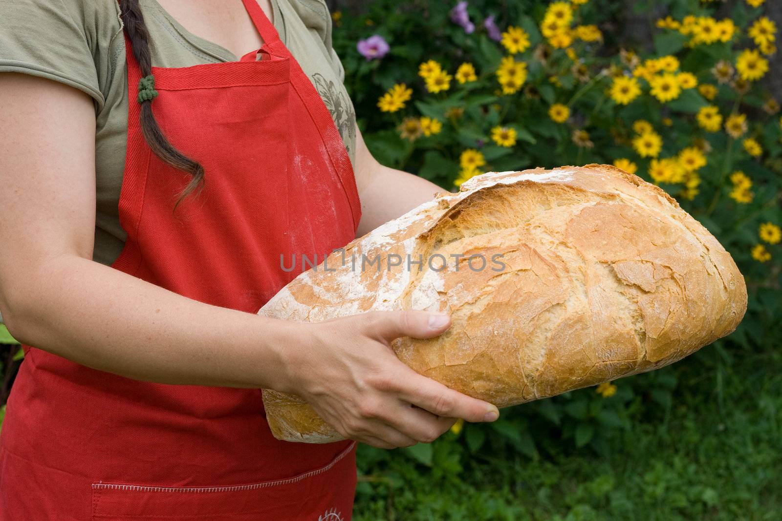 Girl wearing a red pinafore dress holds a hand made freshly baked bread.