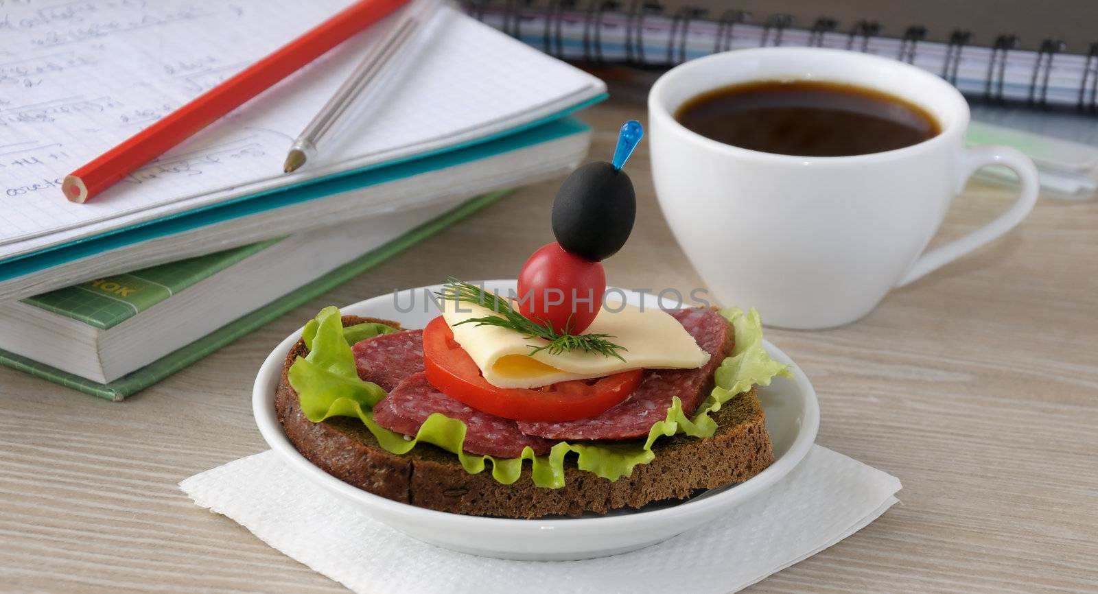 Salami sandwich and a cup of coffee in the background notes and notebooks