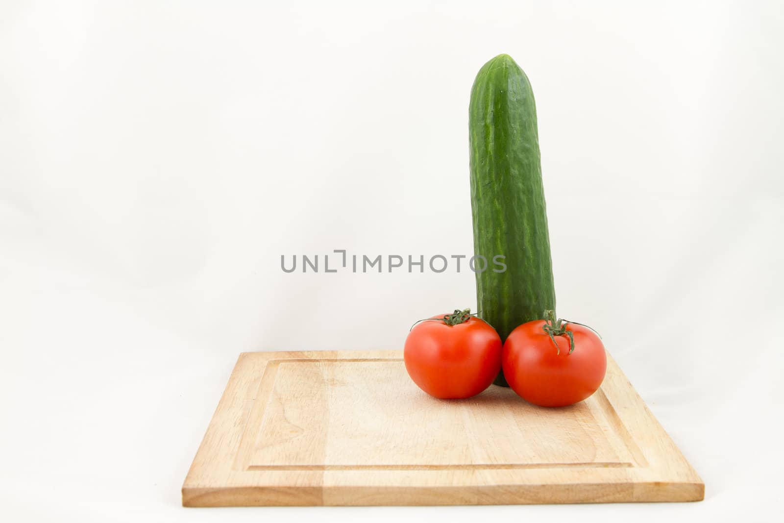 A wooden chopping with a phallic combination of cucumber and tomato isolated on white.