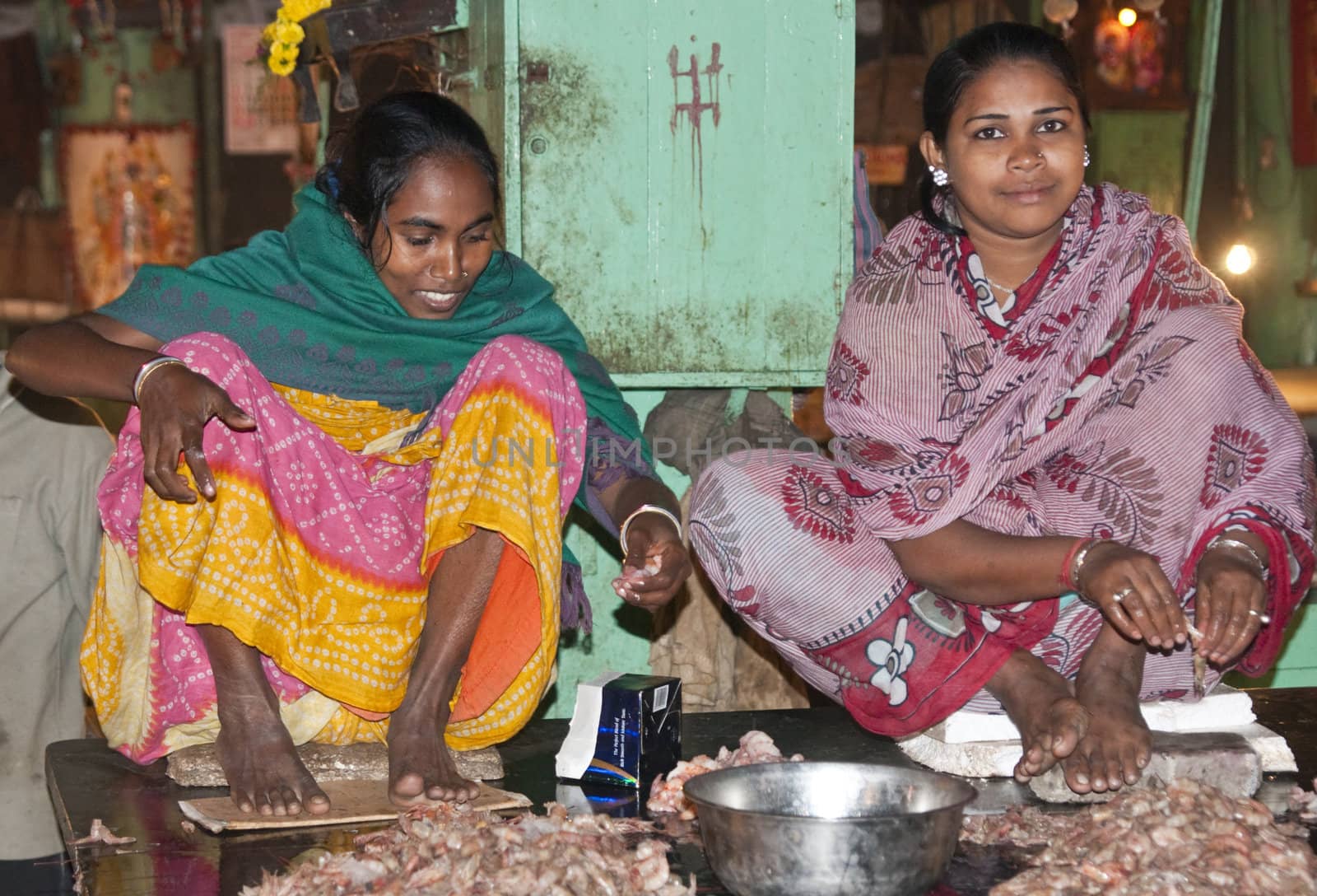 Women in brightly colored sari's shelling prawns in the fish market in Kolkata, West Bengal, India