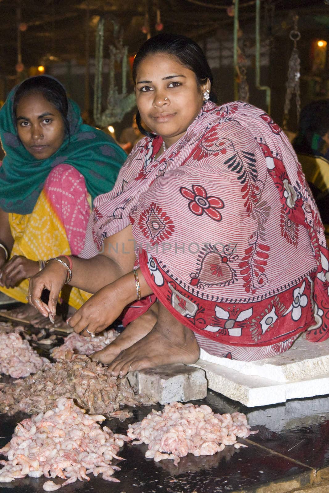 Indian women in brightly colored sari shelling prawns in the fish market in Kolkata (Calcutta), West Bengal, India