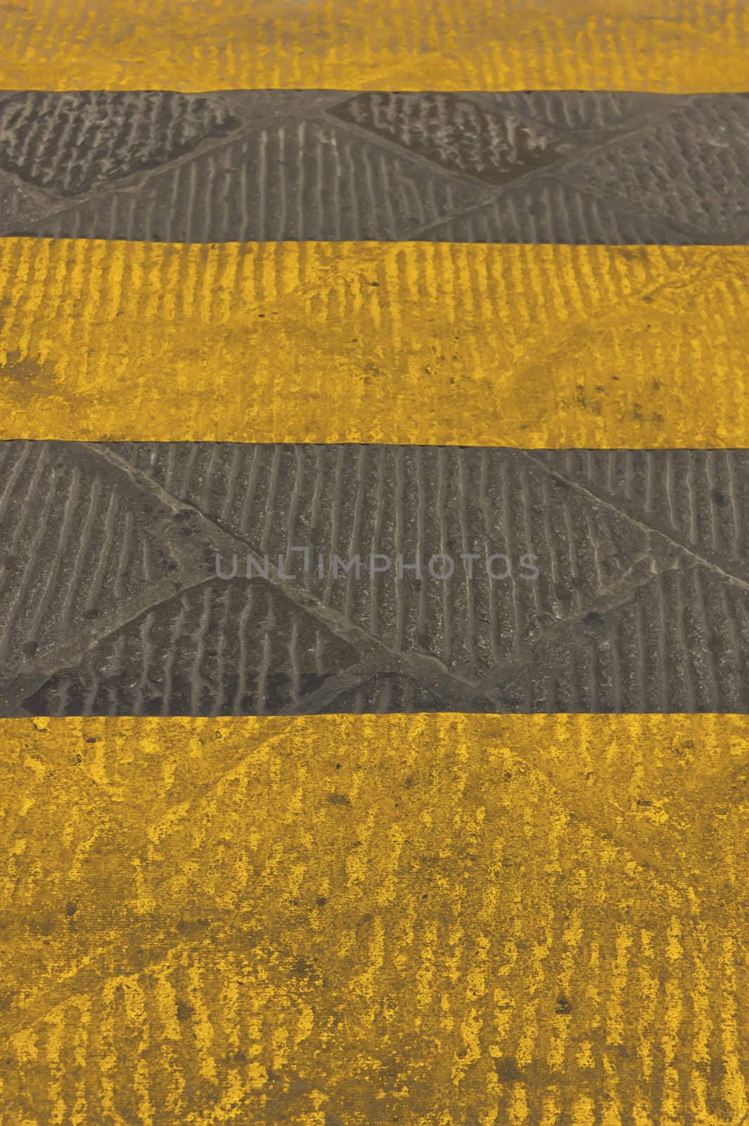 Crosswalk with yellow stripes on stone pavement.