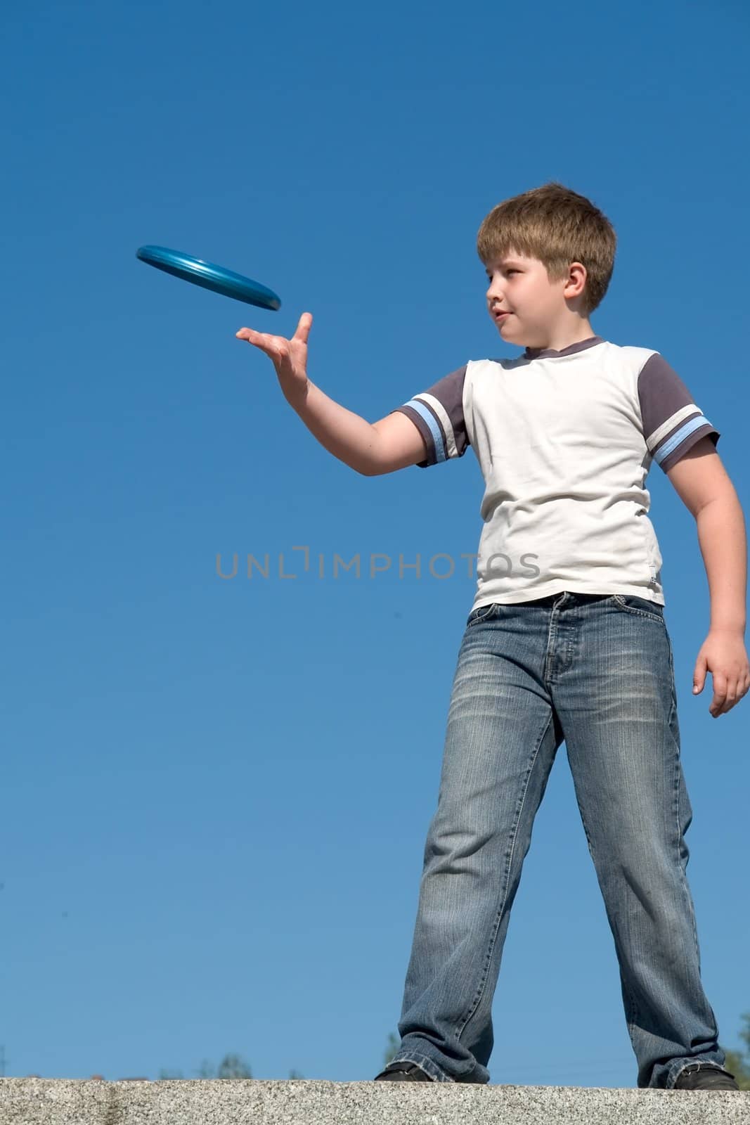 A little boy throws a flying disk with sky at background