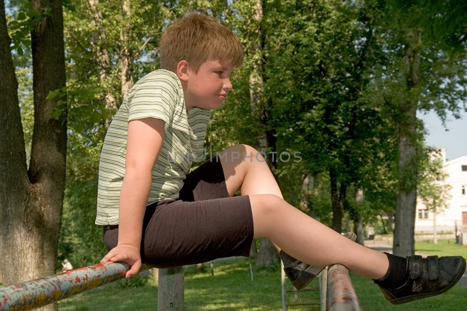 A little boy sits on gymnastic bars