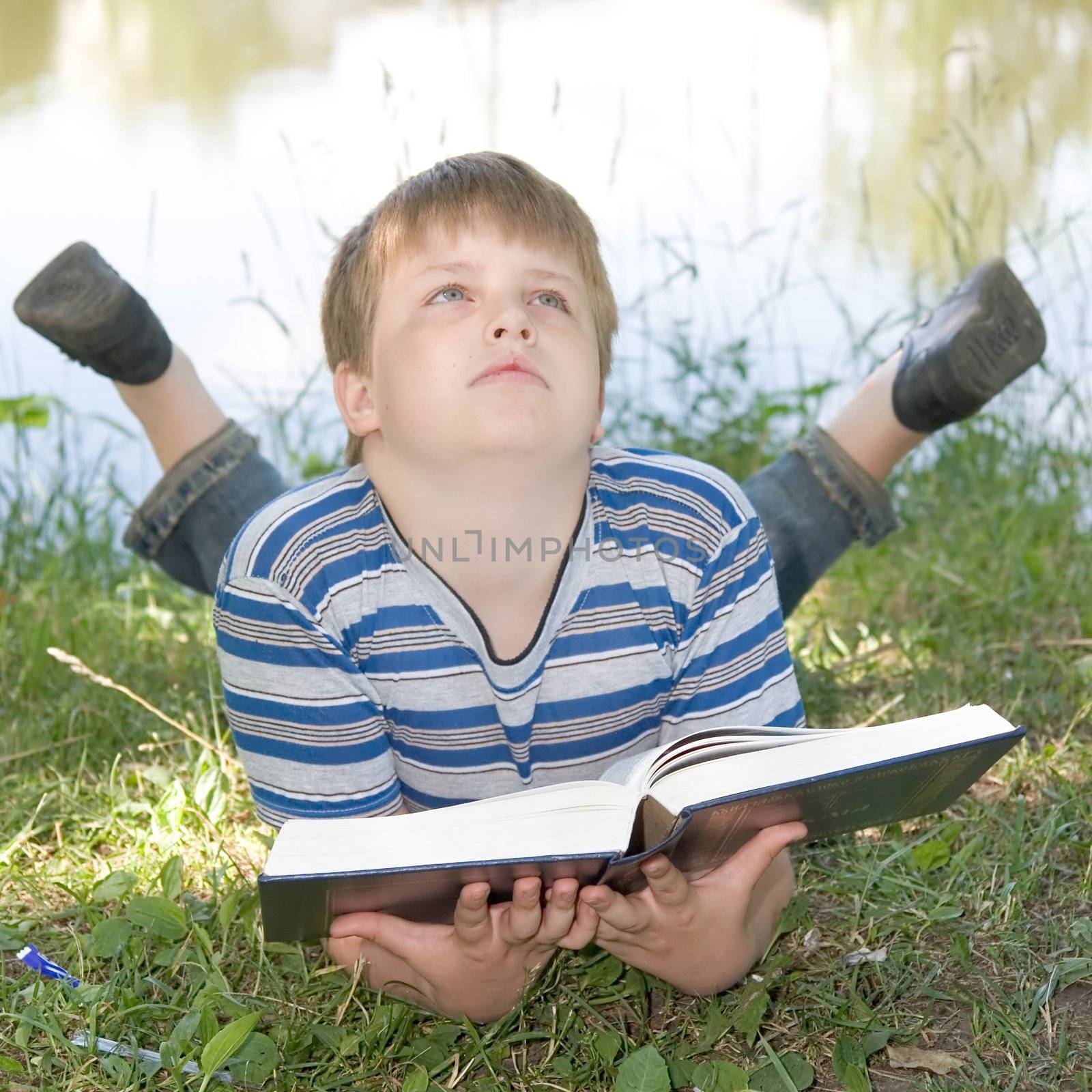 A little boy reads a big book with river at background