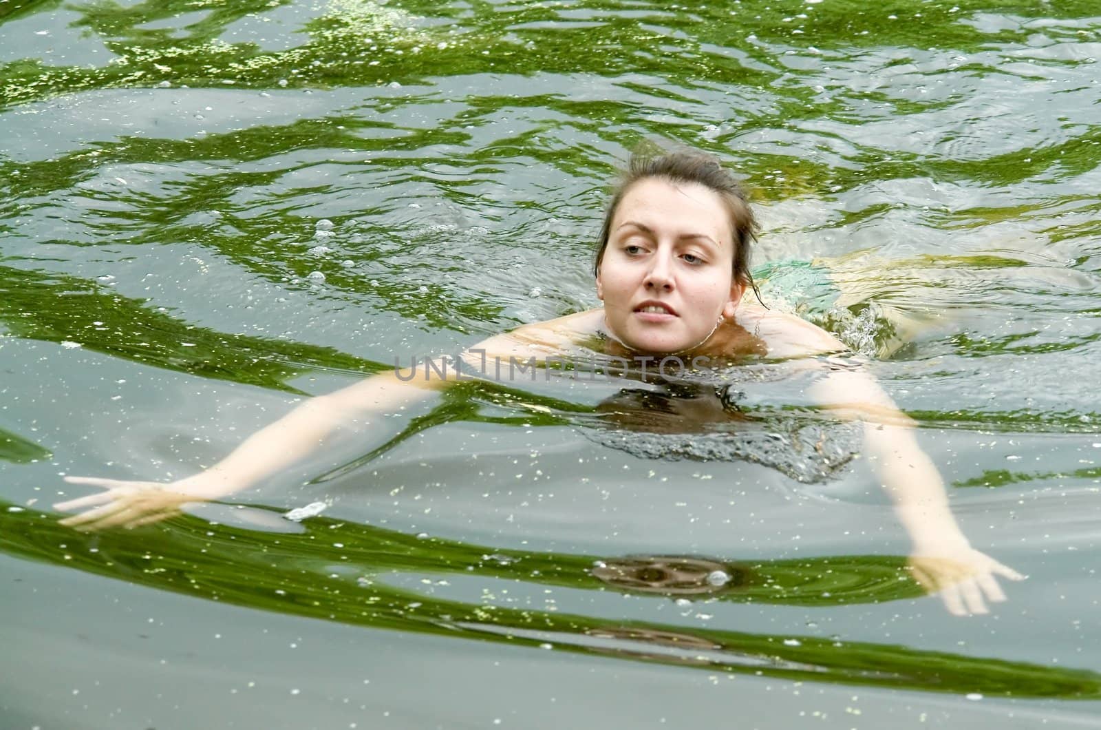 The beautiful girl swims in a green pond