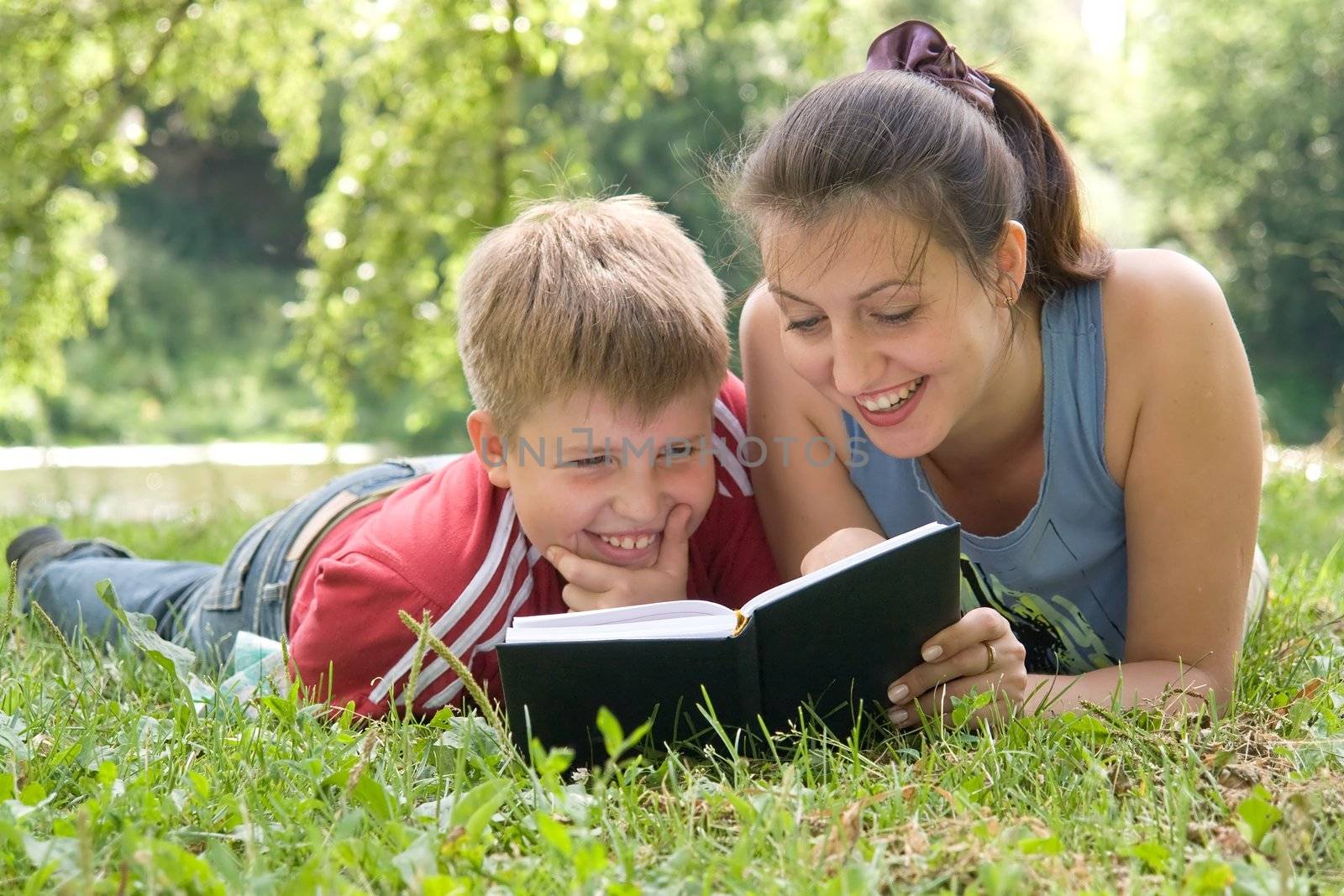 Mum and the son reads the book on a lawn in park