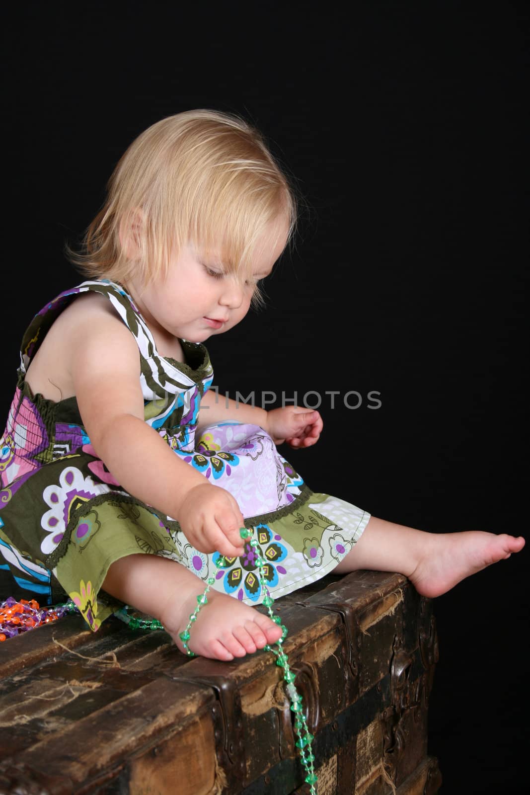 Beautiful blond toddler sitting on an antique trunk playing with beads
