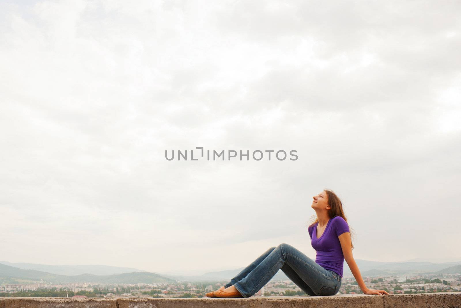 Young woman sitting outdoors against blue sky by AndreyKr