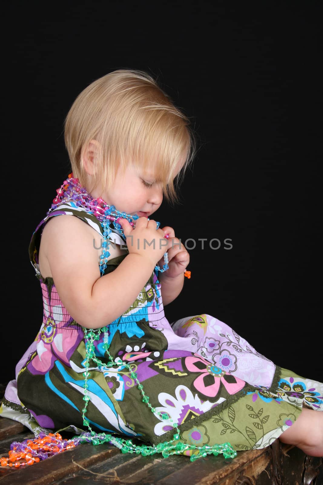 Beautiful blond toddler sitting on an antique trunk playing with beads