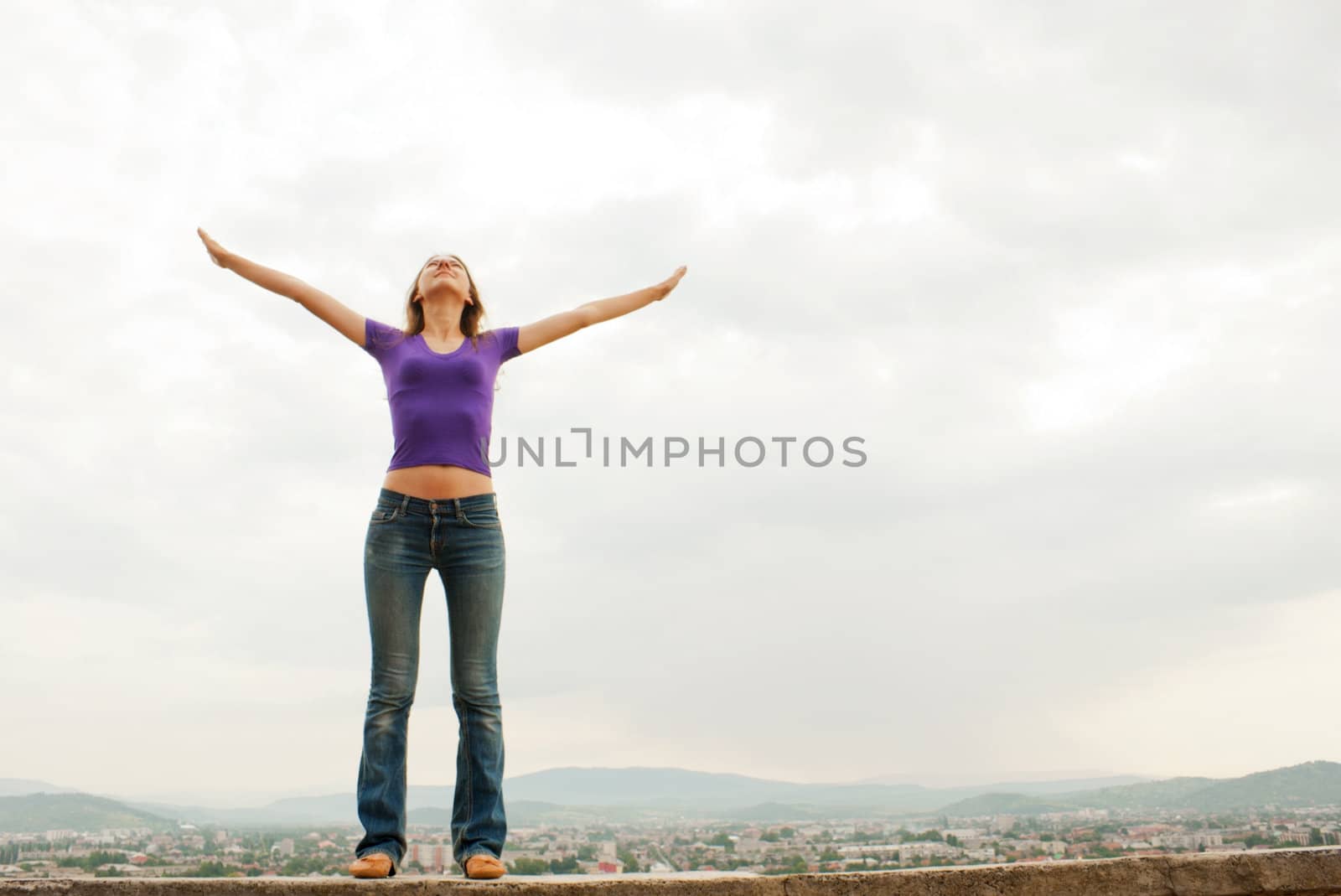 Young woman staying with raised hands against blue sky by AndreyKr