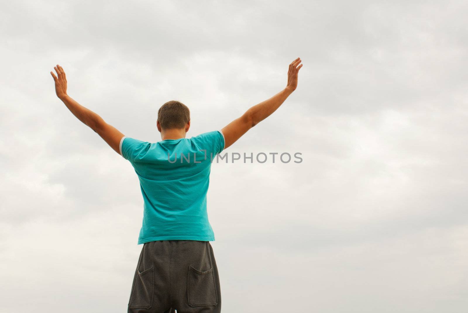 Young man staying with raised hands against blue sky