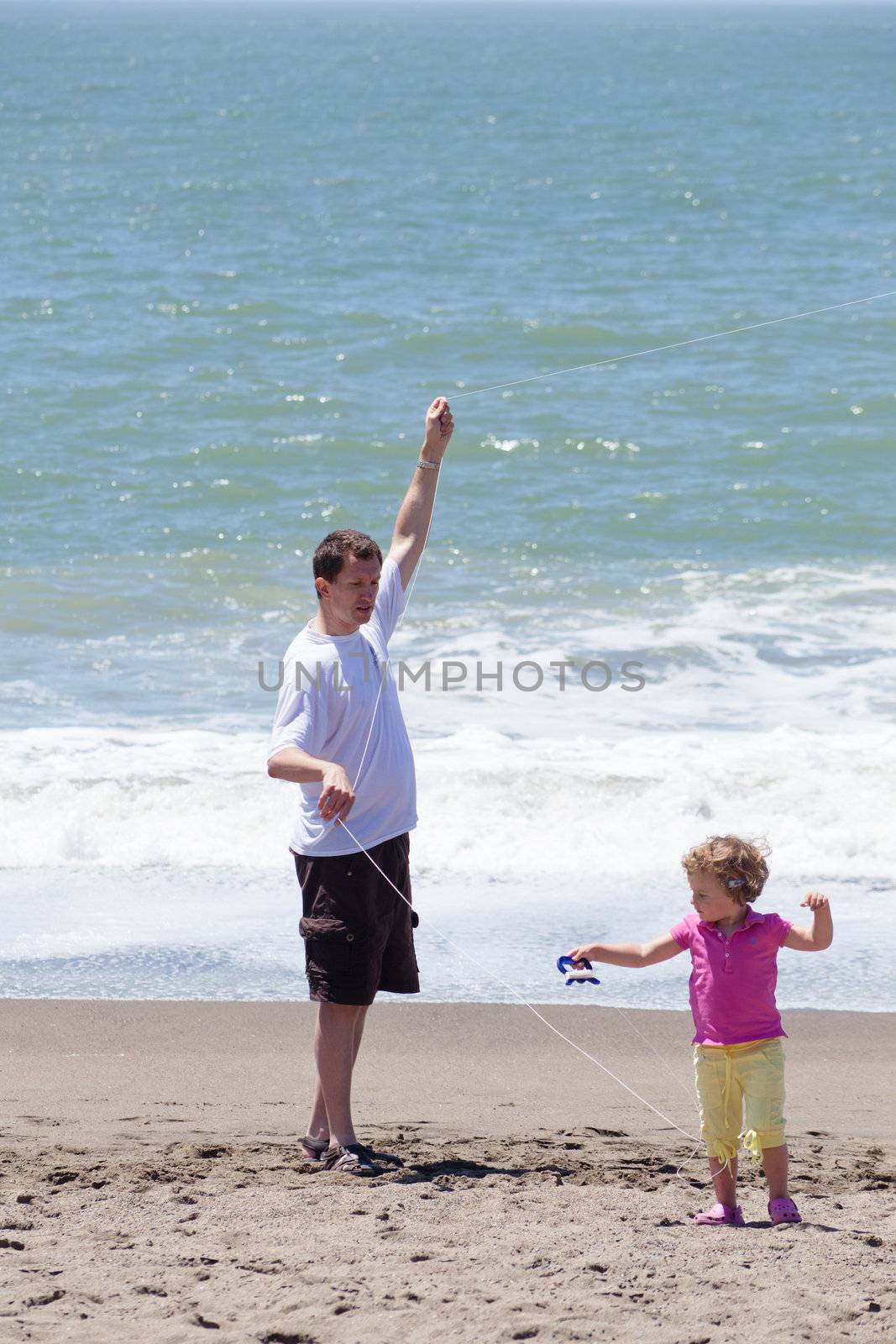 Father and daughter flying kite on the beach on sunny day.