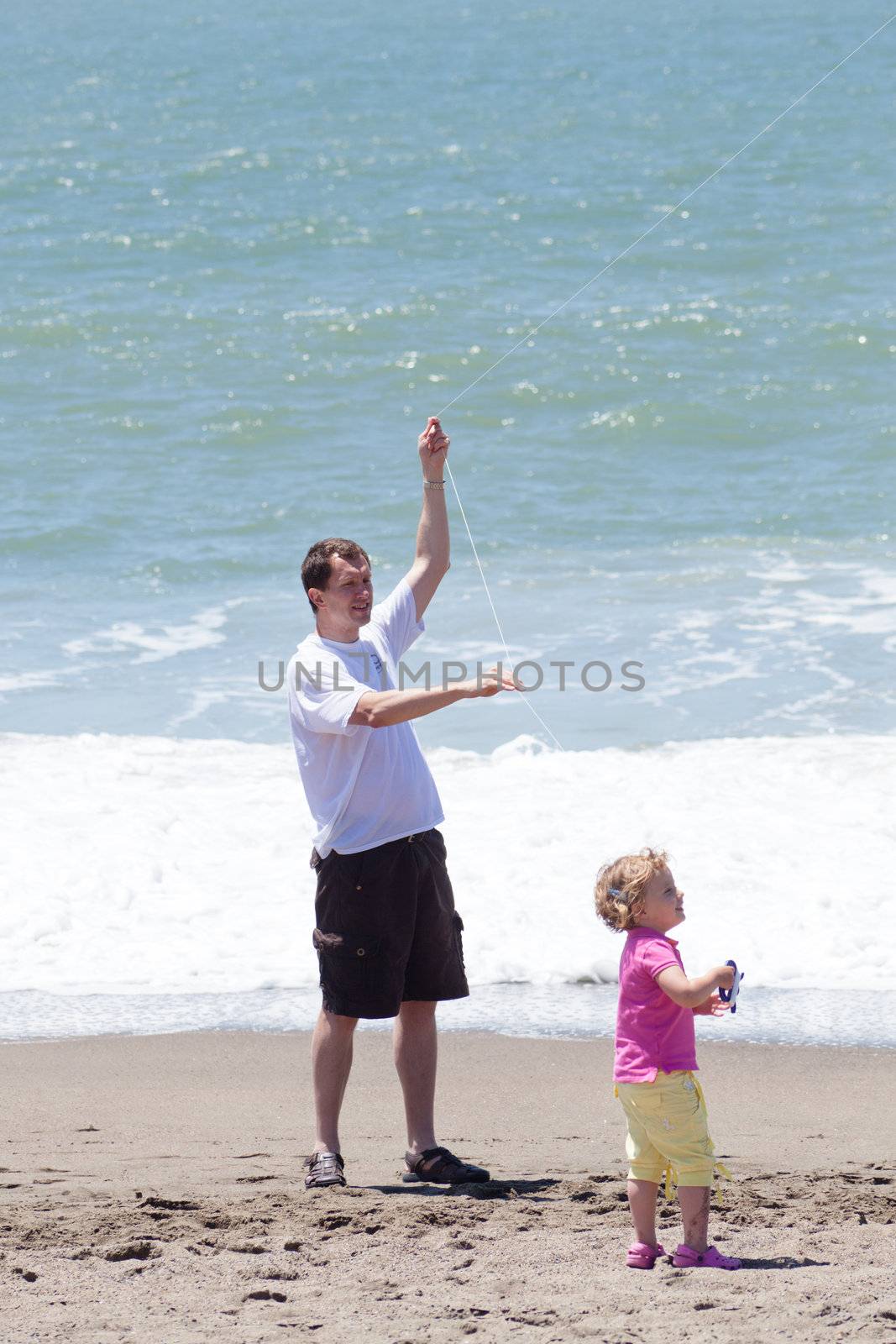 Father and daughter flying kite on the beach on sunny day.