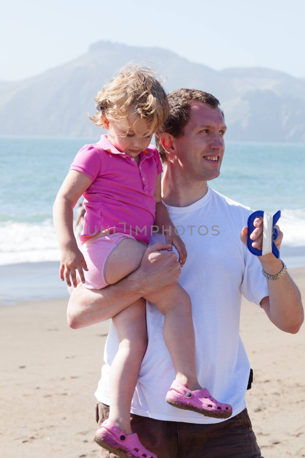 Father and daughter flying kite on the beach on sunny day.