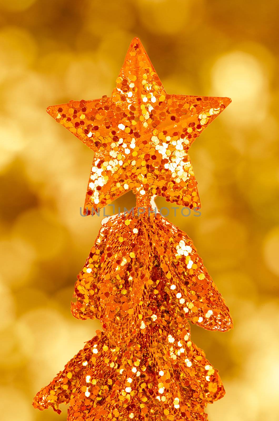 Sequin christmas tree with golden star on top over defocussed lights in the background.