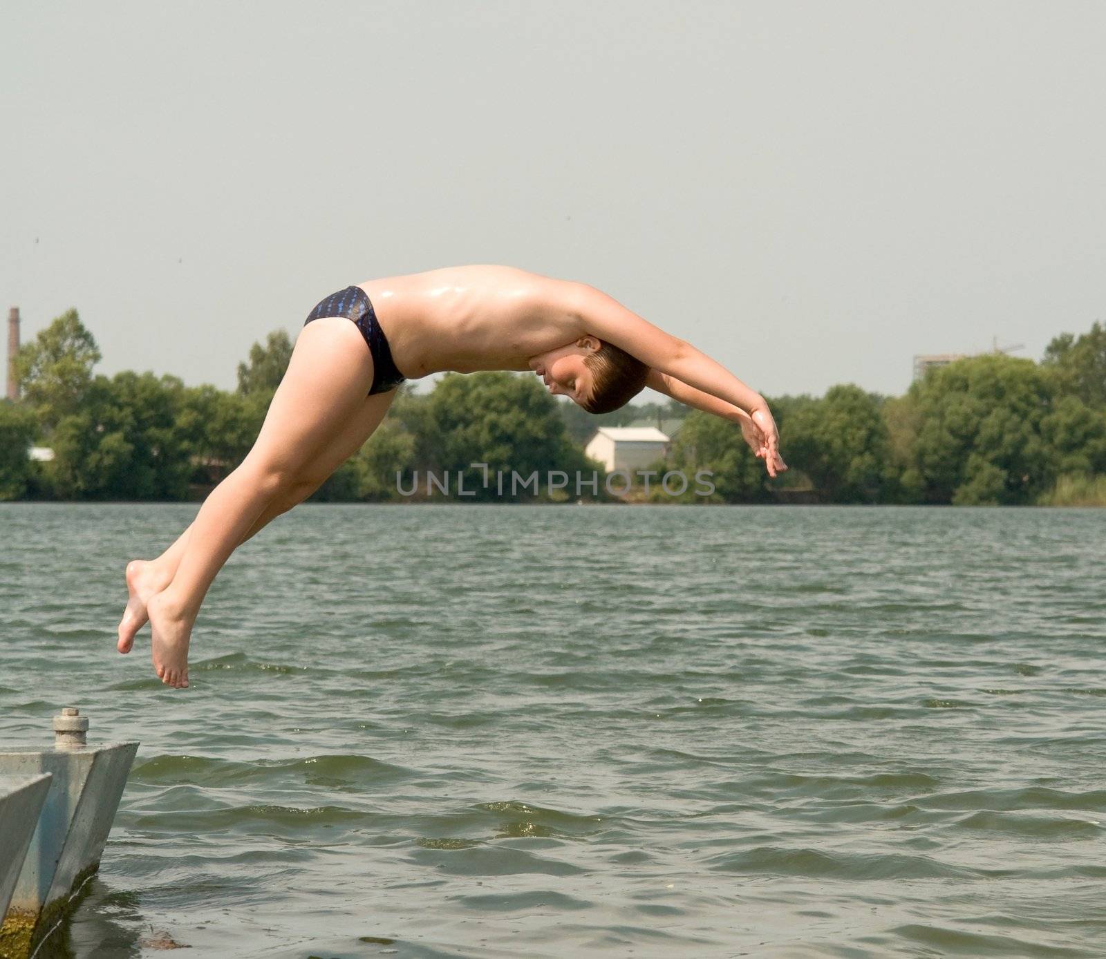 The little boy jumps from a pier in water