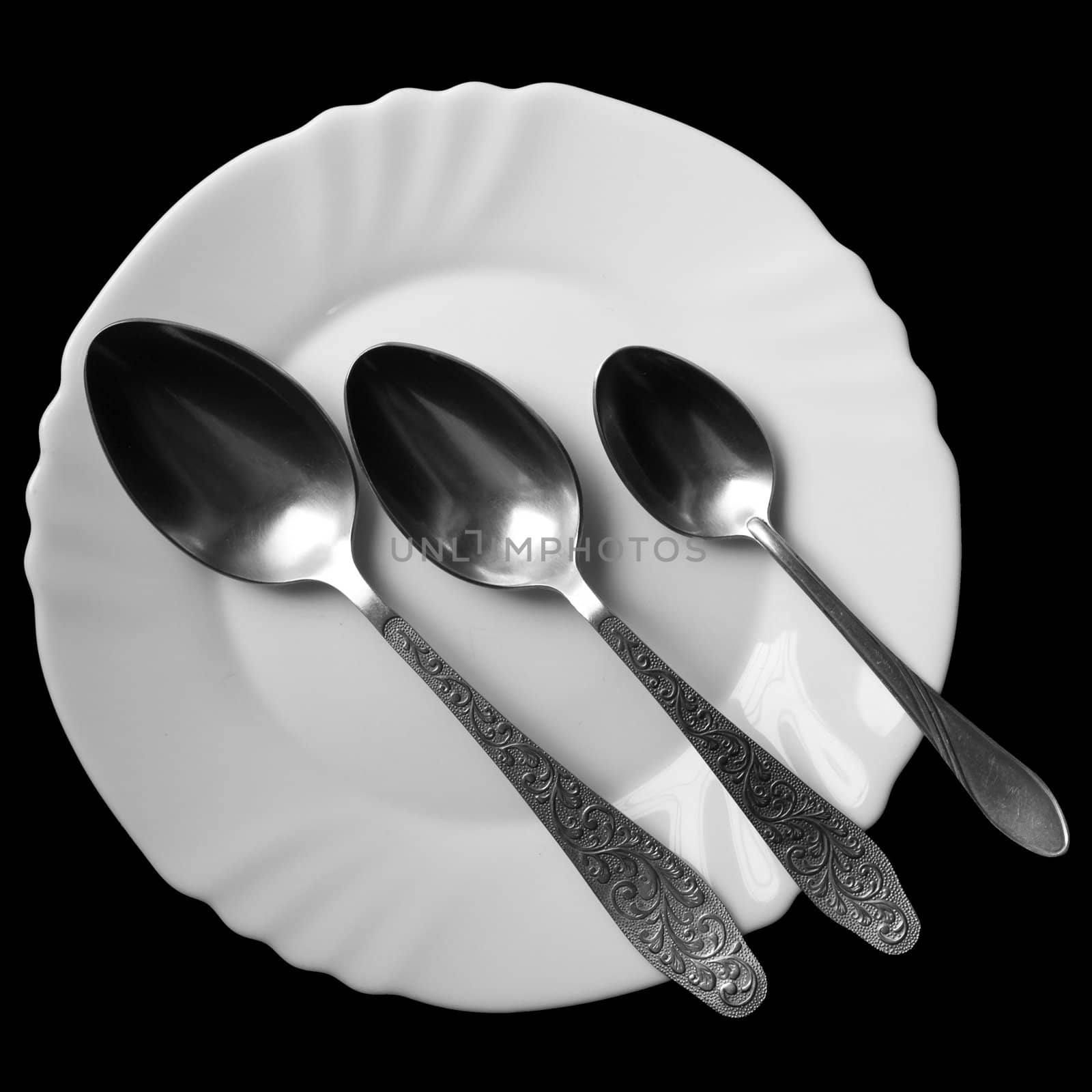 Three spoons on a white plate on a black background