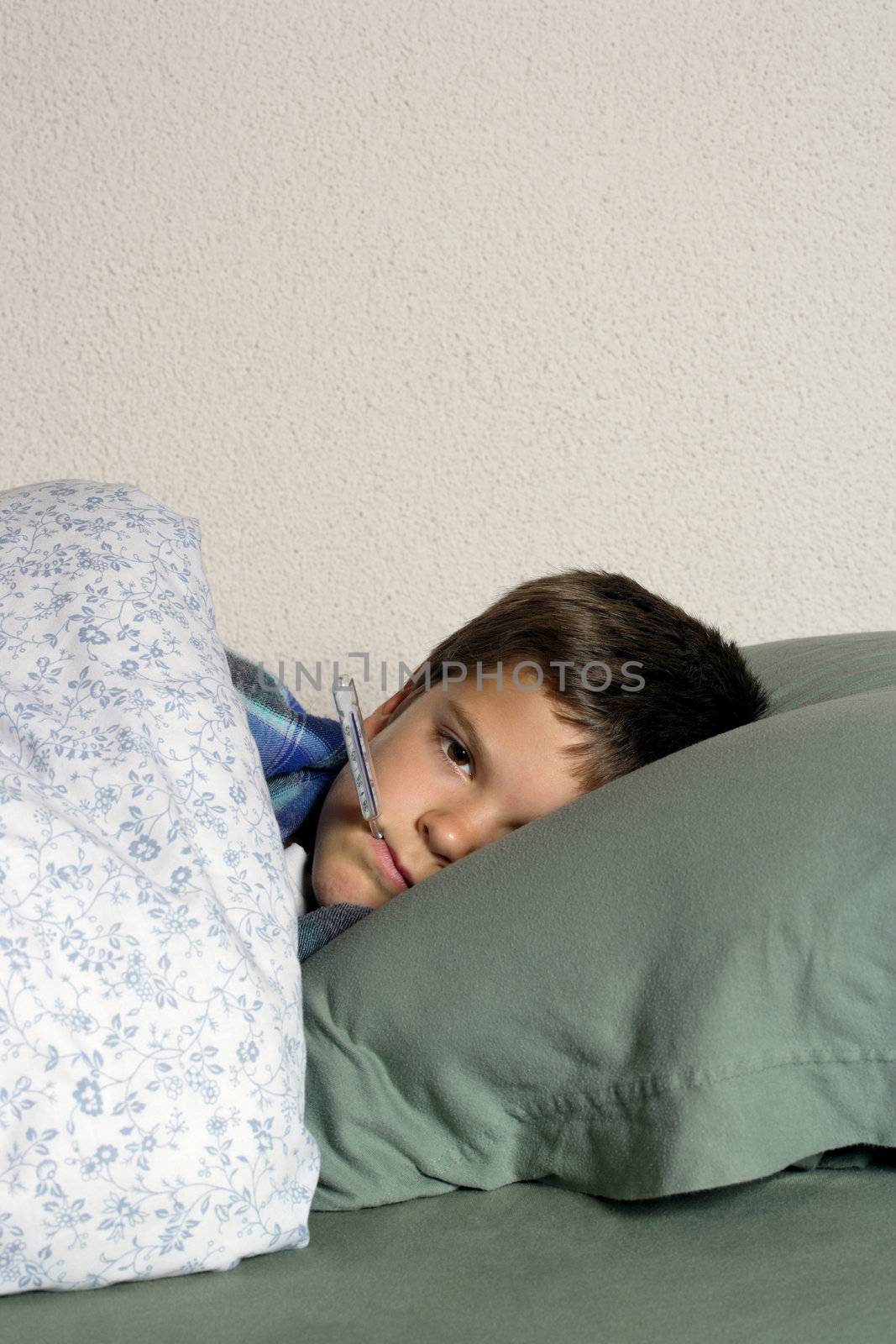 Sick child with thermometer, frustrated at his illness, resting in bed.
