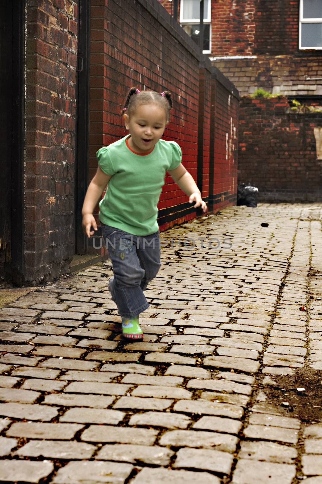 Young black baby girl playing on cobble stoned alley