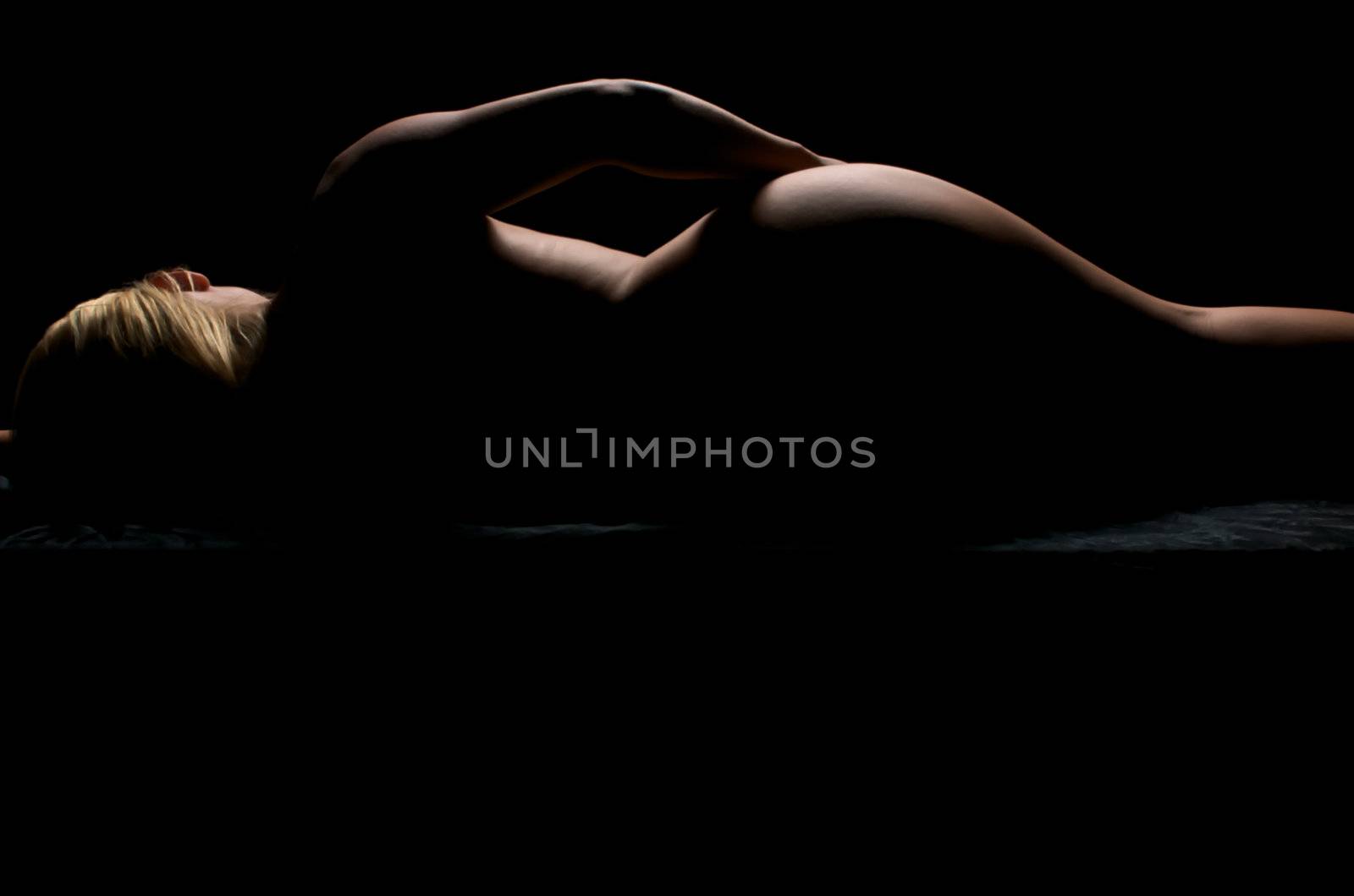 Sensual blonde posing nude in dim light.