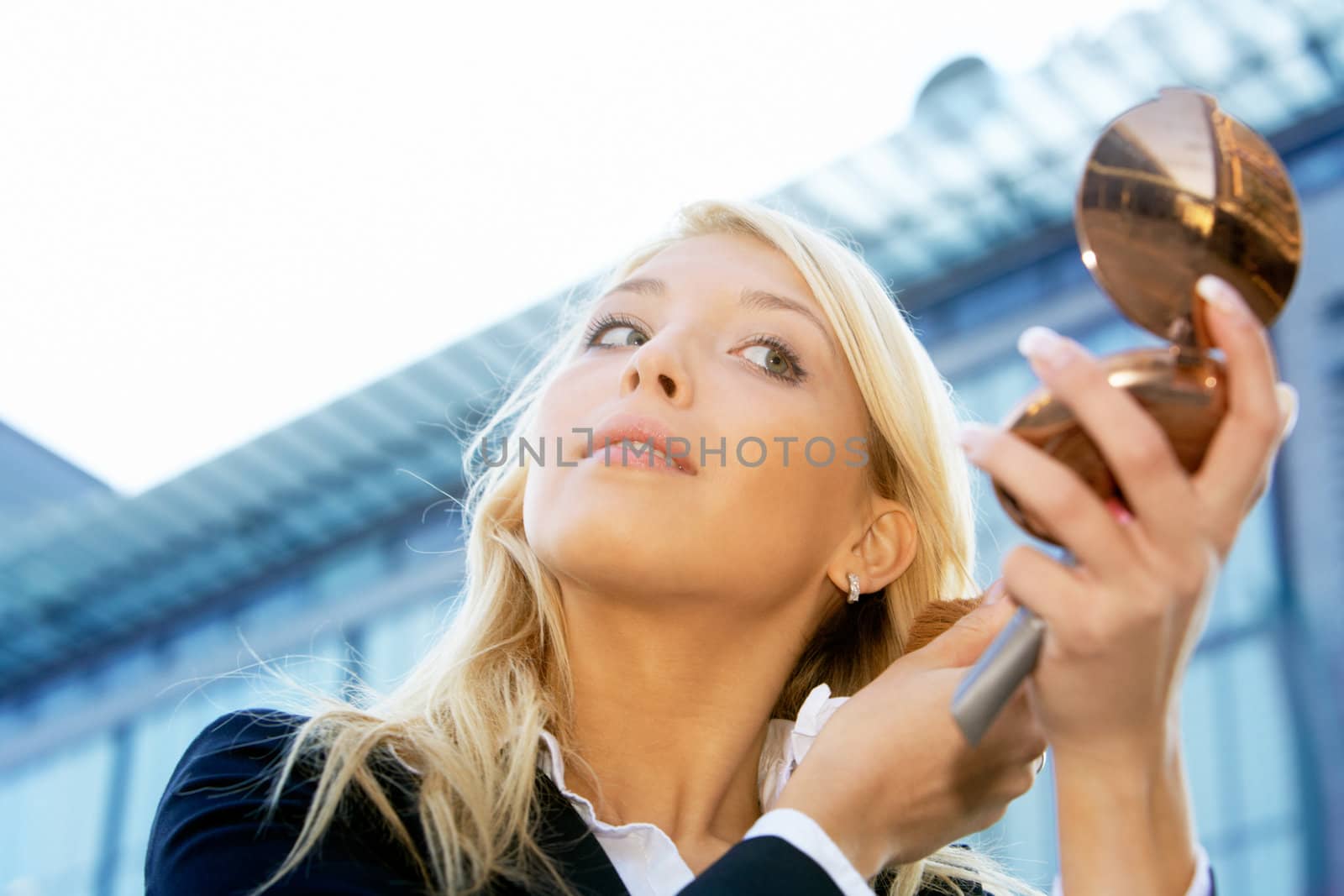 Businesswoman applying make-up outdoors in city, low angle view