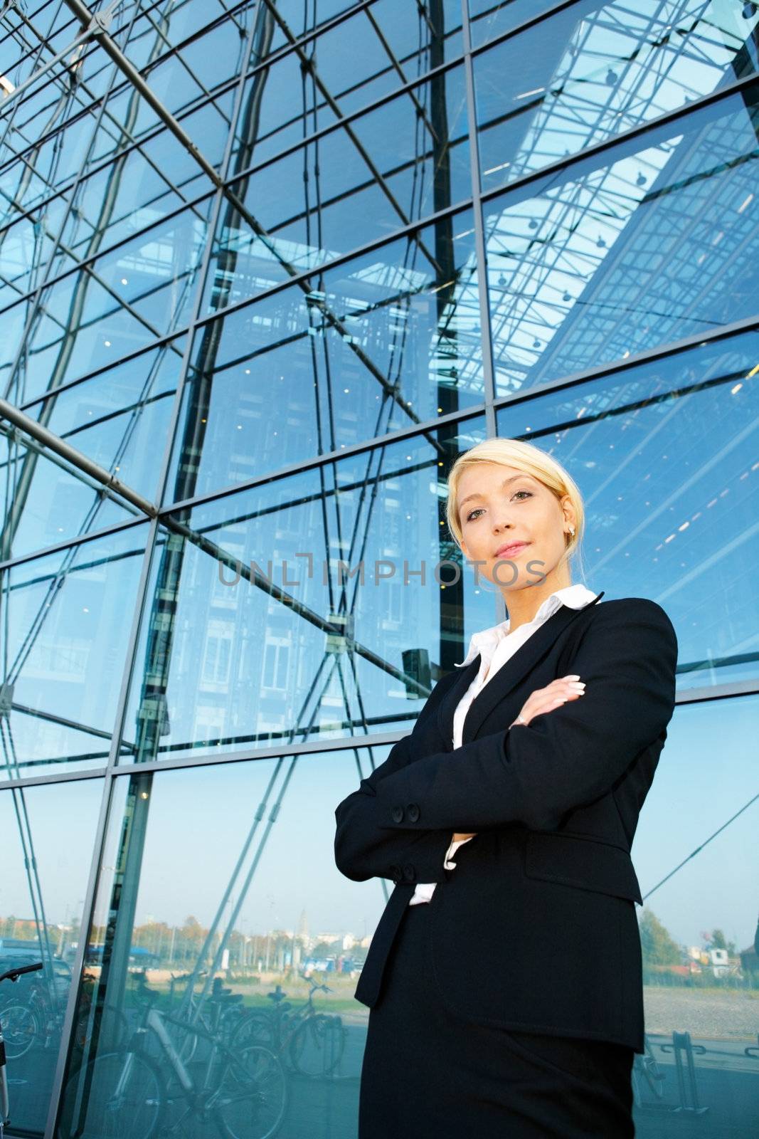 Young businesswoman standing by building arms crossed, wide angle view