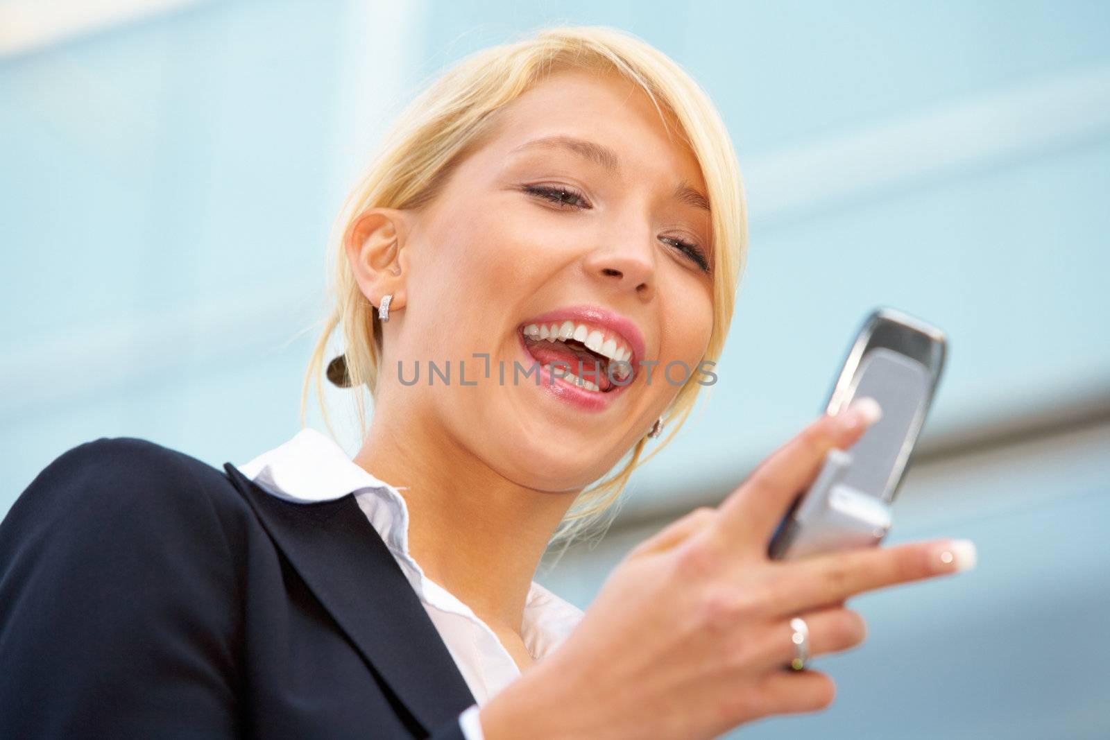 Young businesswoman looking at mobile phone outside office building