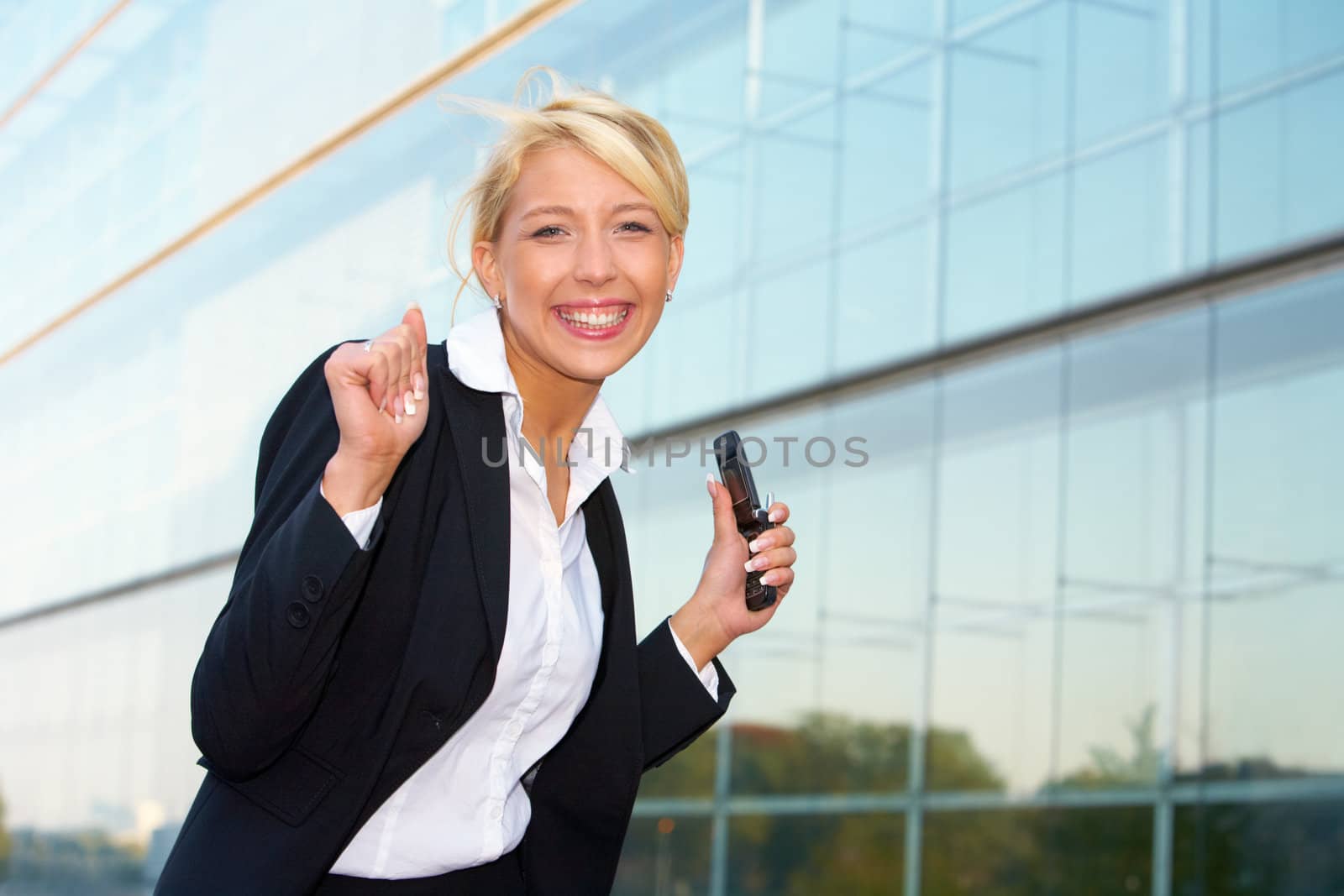 Young businesswoman looking at camera outside office building, holding mobile phone