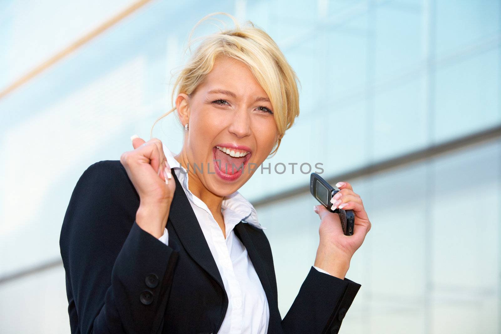 Young businesswoman looking at camera outside office building, holding mobile phone