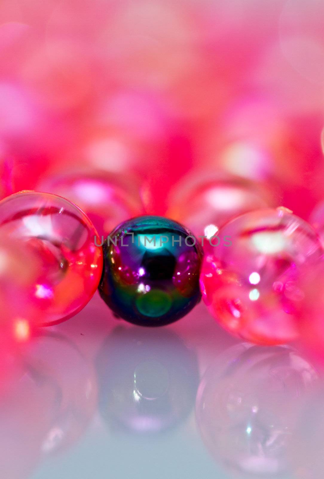 one dark green bead surrounded by red beads on reflecting white surface