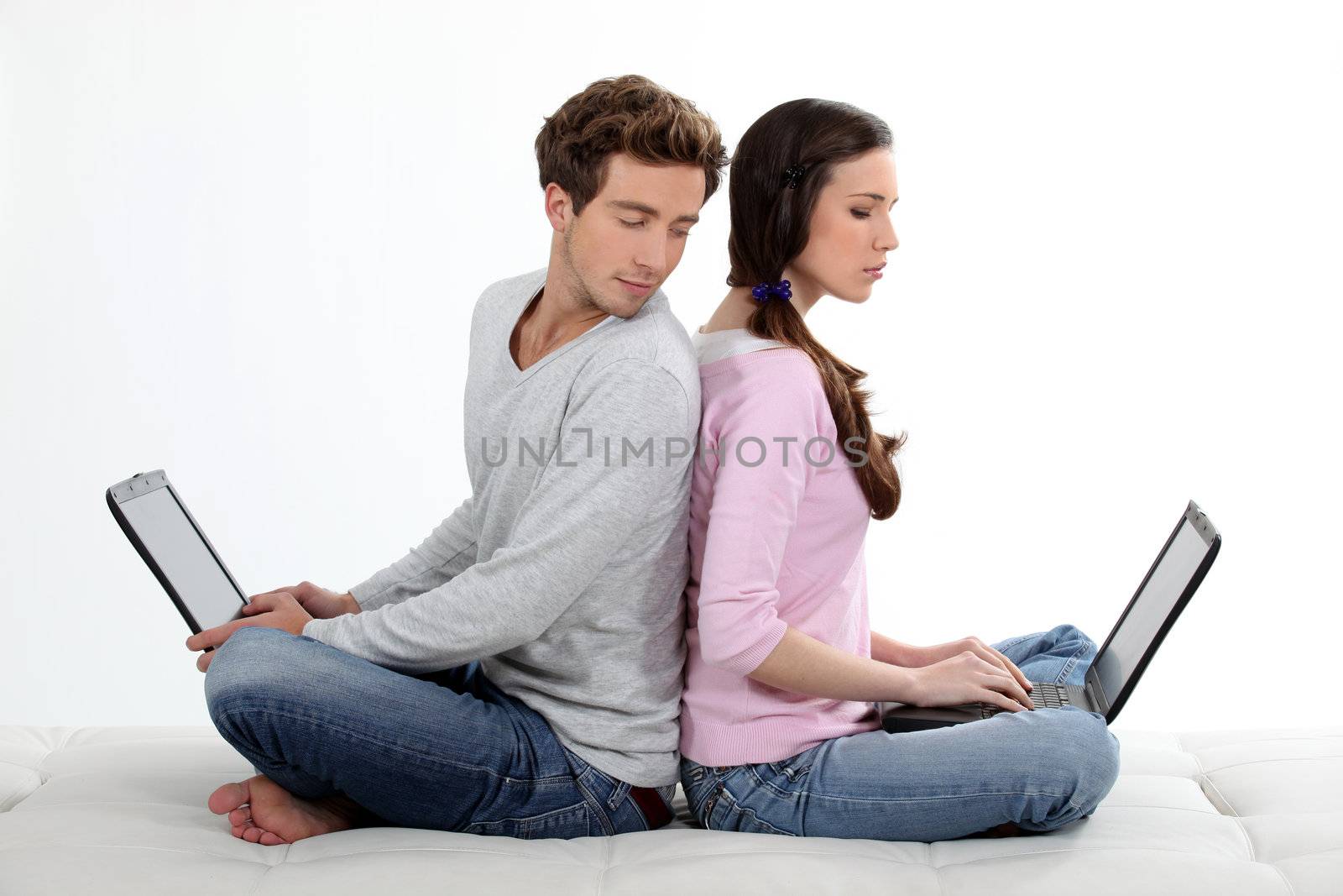 portrait of lovely young couple back-to-back with laptop by phovoir