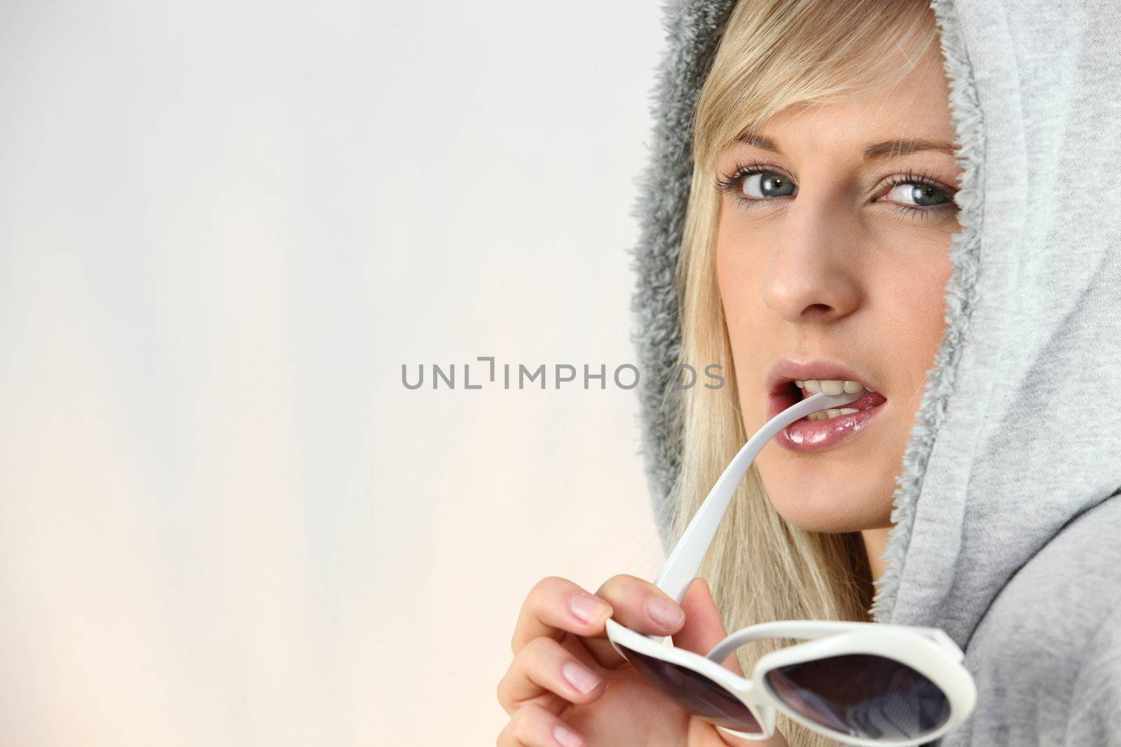 Woman with a hood on and chewing on her sunglasses