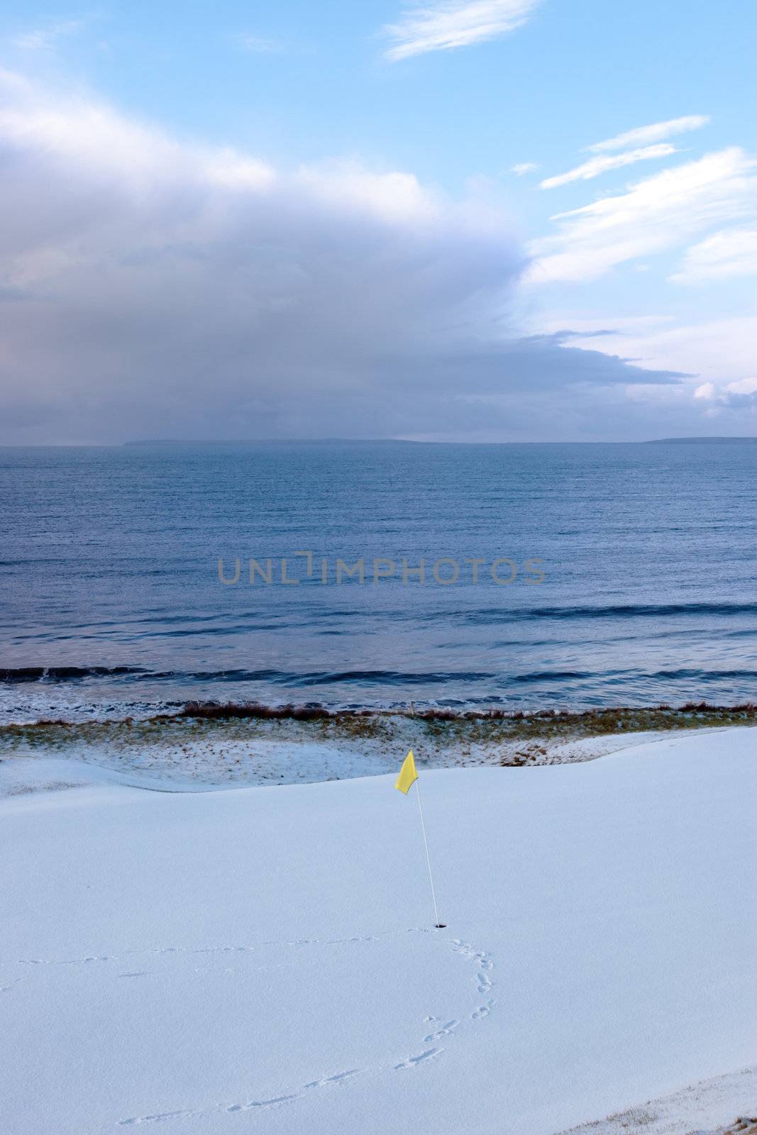 a snow covered links golf hole in ireland in winter weather with yellow flag