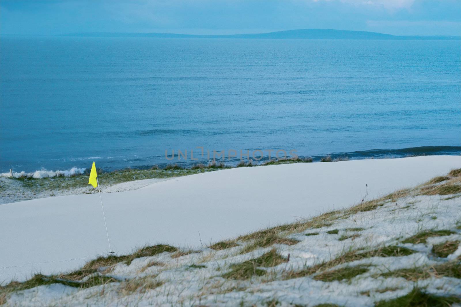a snow covered links golf hole in ireland in winter weather with yellow flag