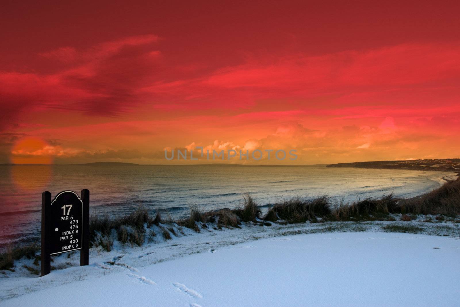 a snow covered links golf hole in ireland with seventeen tee sign and orange sunset sky
